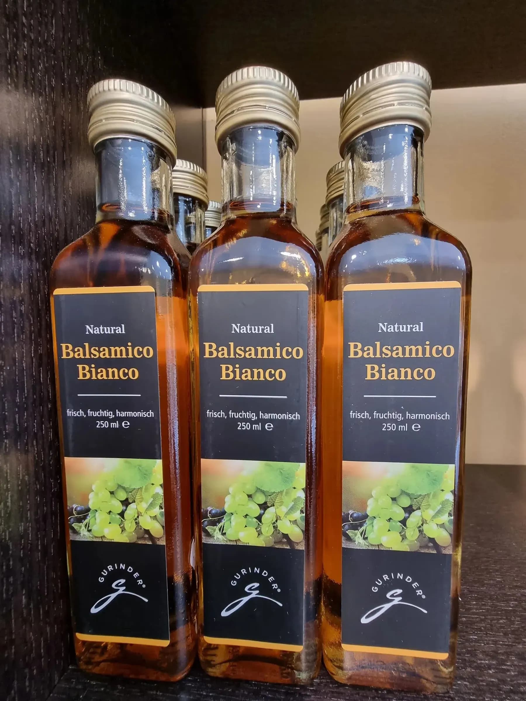 Drei Flaschen Balsamico Bianco auf einem dunklen Holzregal