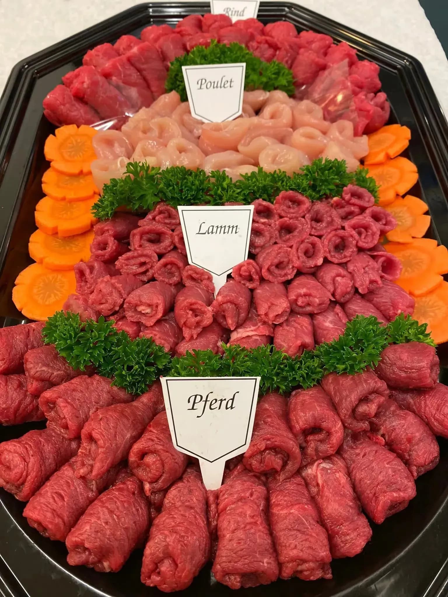 Tablett mit gerollten Fleischstücken, beschriftet mit Pferd, Lamm, Poulet und Rind